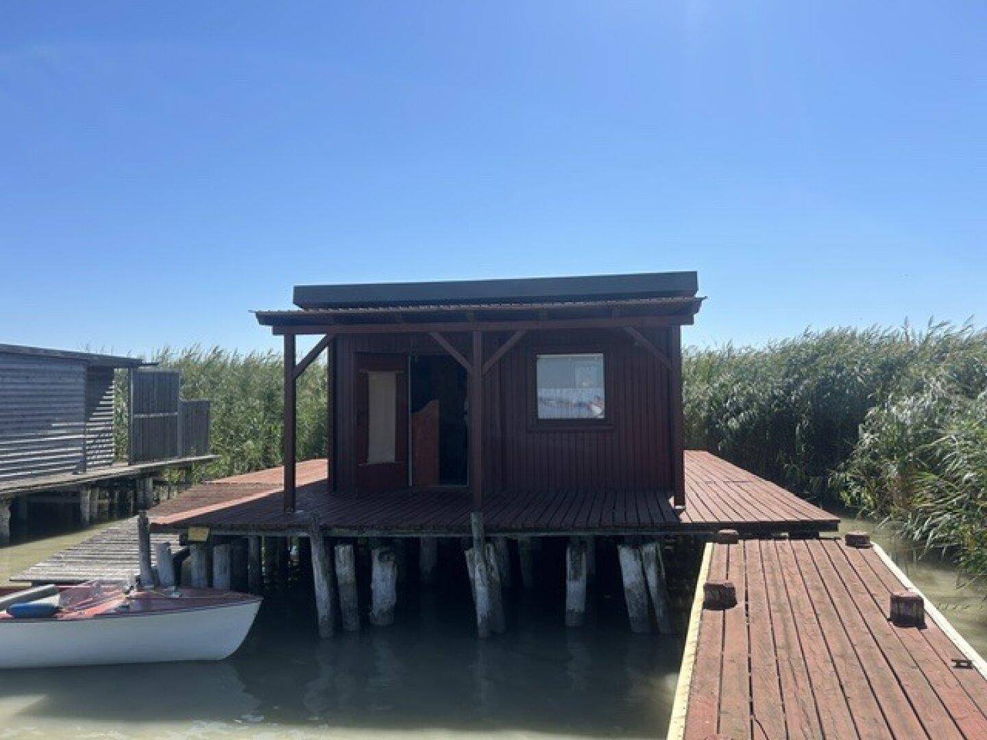 Rustikale Holzhütte auf Stelzen mit einer Holzterrasse und einem kleinen Boot am Ufer eines Sees.