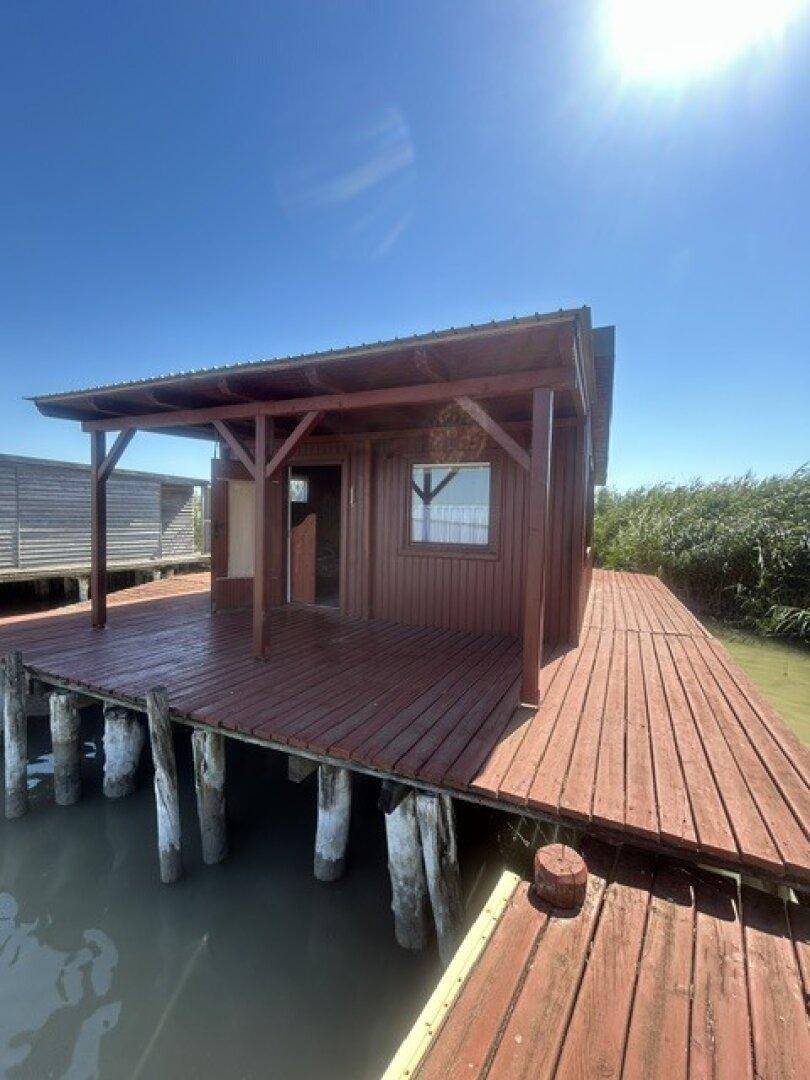 Kleine Holzhütte auf Stelzen über dem Wasser mit einer einladenden Holzterrasse unter strahlendem Sonnenschein.