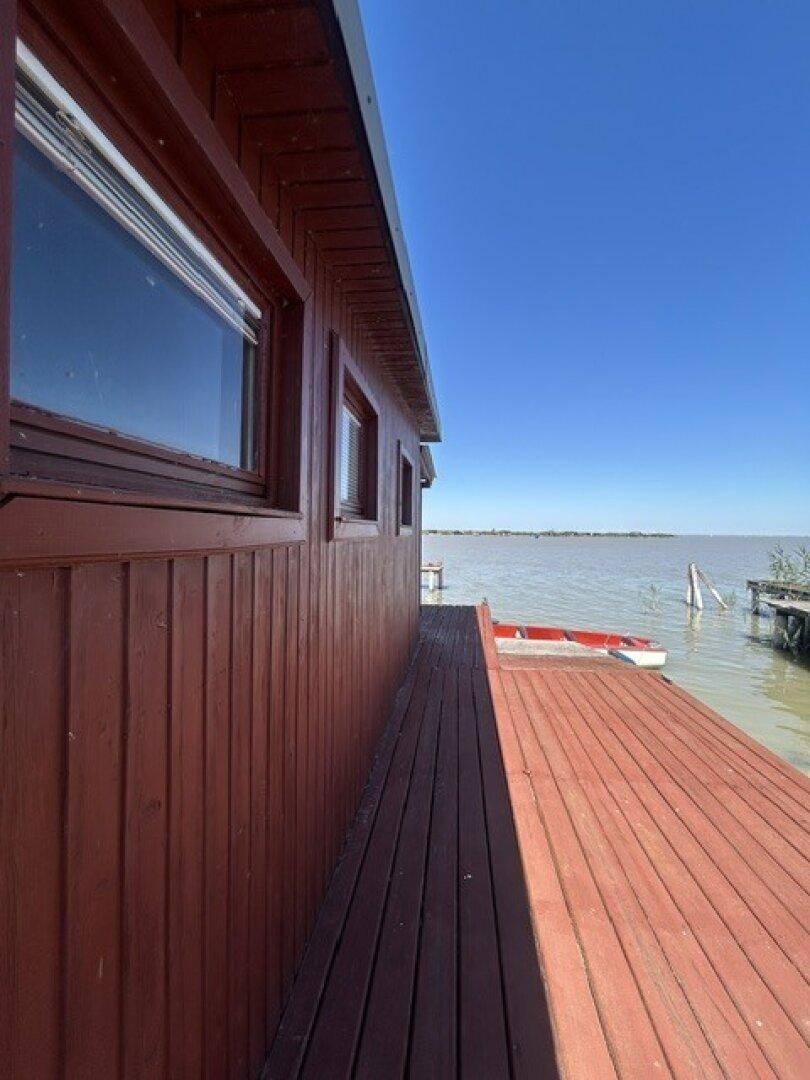 Seitliche Ansicht der Holzhütte mit Fenstern und Holzsteg, der zum Seeufer mit einem Boot führt.