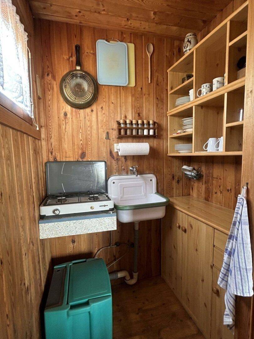 Funktionale Küchenzeile mit Gasherd, Spülbecken und offenen Holzregalen in rustikalem Ambiente.