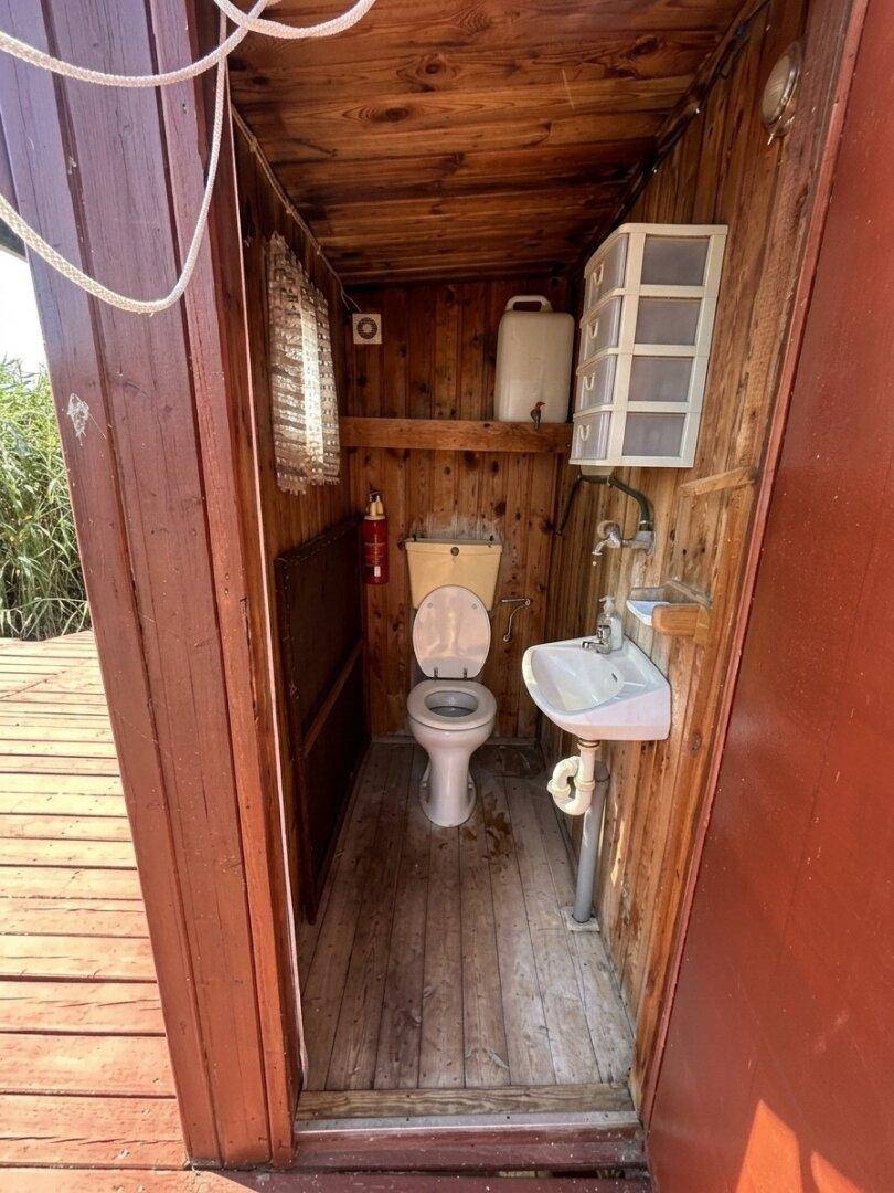 Einfaches WC mit Holzwänden, Toilette und kleinem Waschbecken in rustikalem Stil.