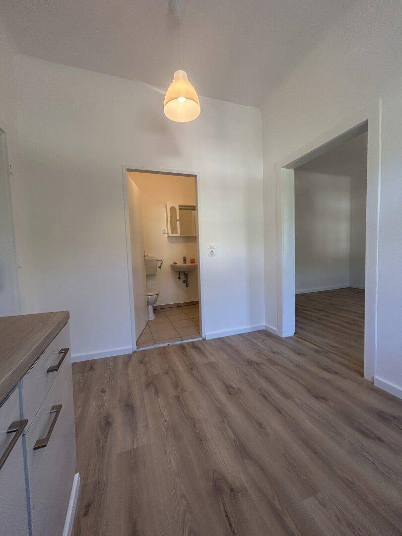 Heller Flur mit Laminatboden und Zugang zu einem Badezimmer und einem weiteren Raum.