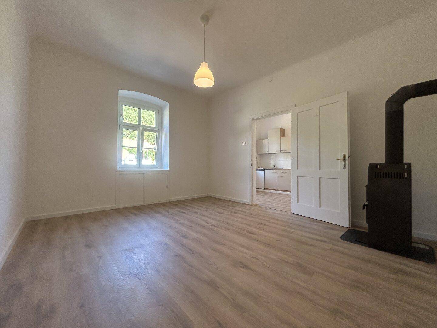 Geräumiger, heller Raum mit Laminatboden, Kaminofen und Zugang zu einem weiteren Zimmer.