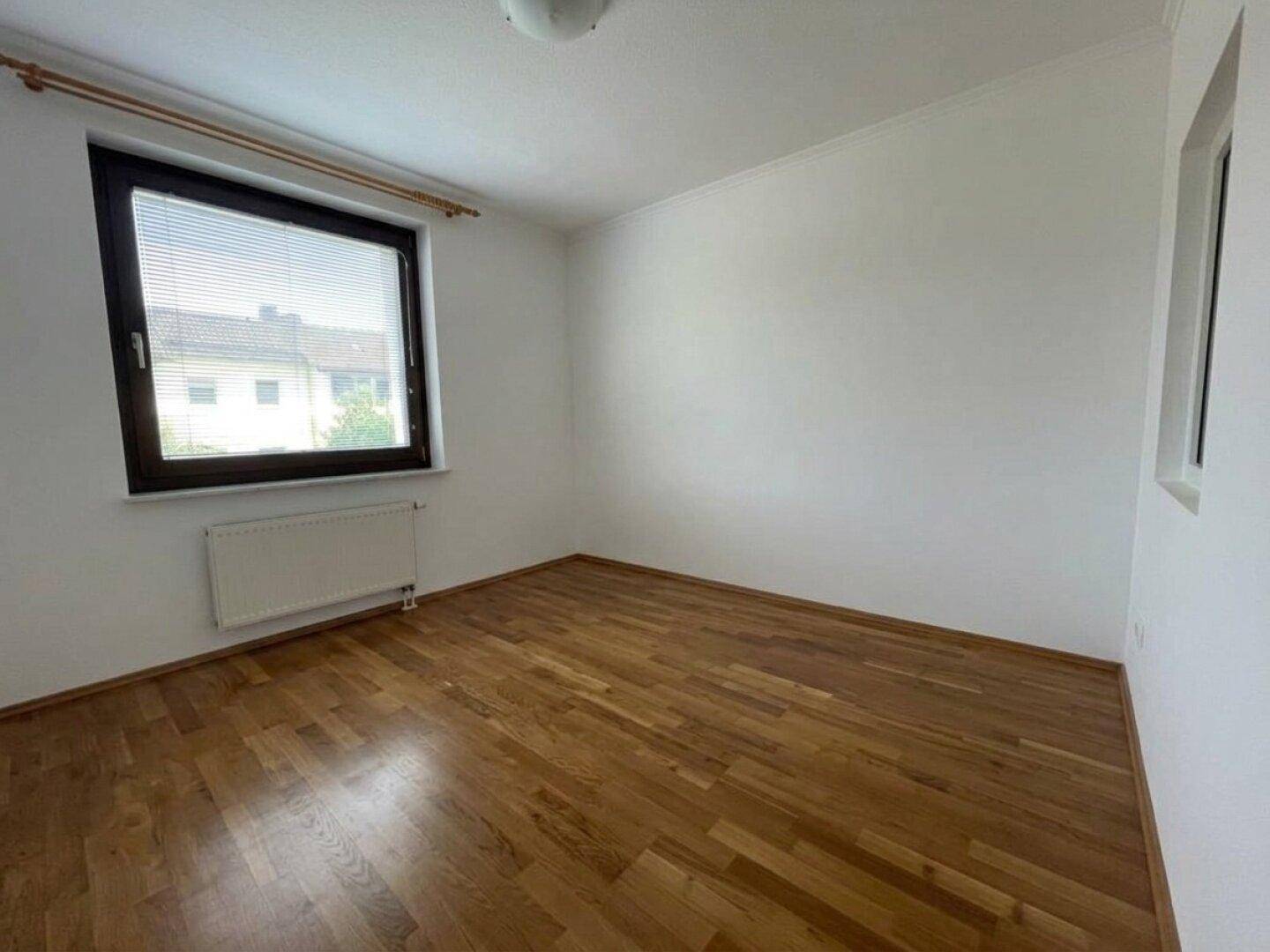 Helles Schlafzimmer mit Parkettboden und zwei Fenstern für viel Tageslicht.