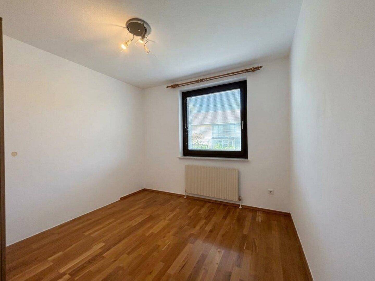 Helles Schlafzimmer mit Parkettboden und Fenster mit Blick ins Grüne.