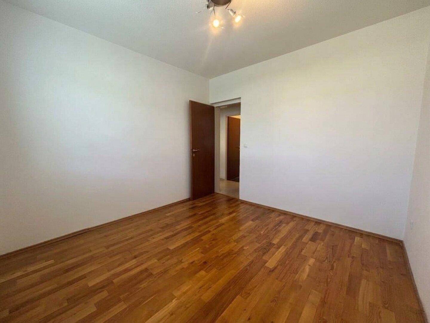 Schlafzimmer mit Parkettboden und Zugang zu einem Flur.