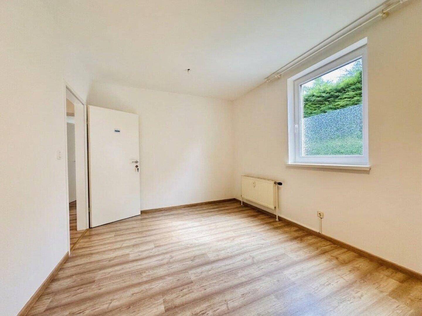 Helles Zimmer mit Laminatboden, Fenster und Heizkörper, ideal als Schlaf- oder Arbeitszimmer.