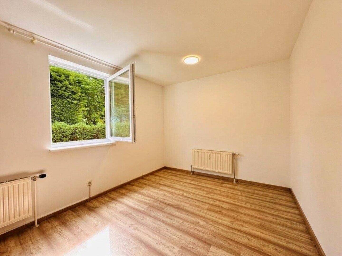 Helles Zimmer mit Laminatboden, großem Fenster und Blick ins Grüne.