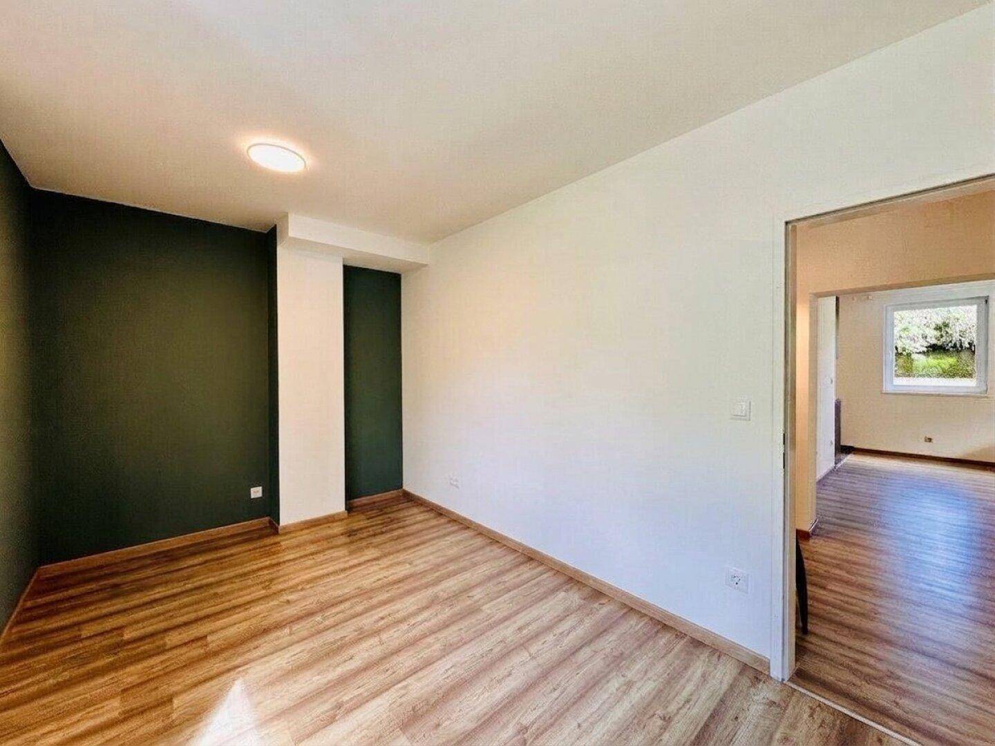 Geräumiger Wohnbereich mit Laminatboden und einer dunkelgrünen Akzentwand.