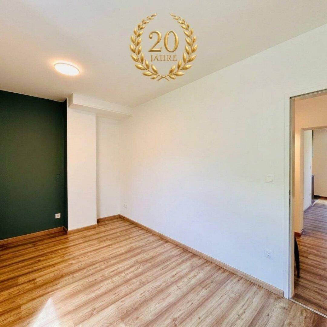 Heller Wohnraum mit Laminatboden und einer Akzentwand in dunklem Grün.