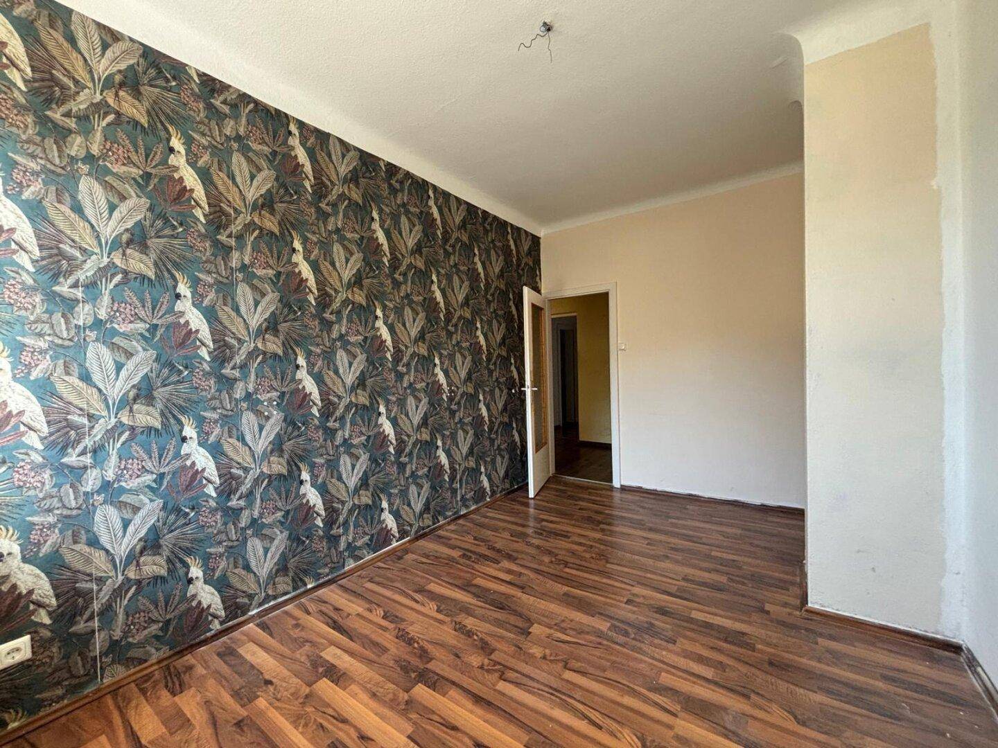 Geräumiges Zimmer mit Laminatboden und exotischer Tapete, ein Durchgang führt zu einem weiteren Raum.