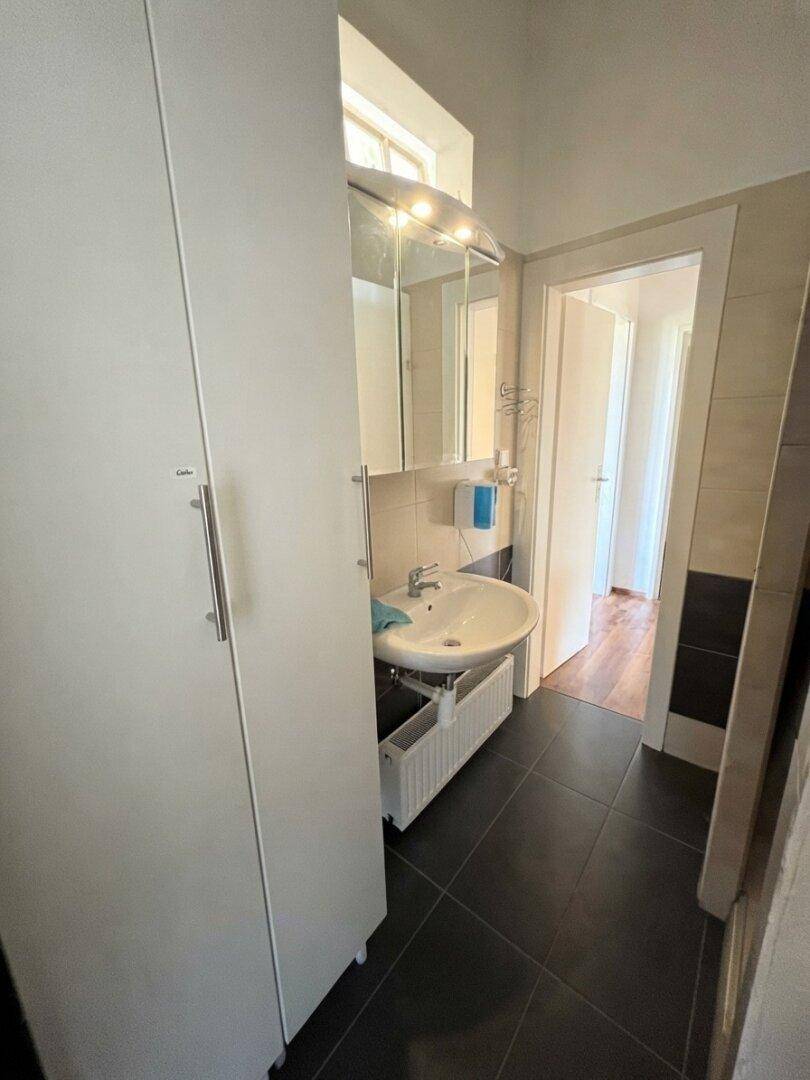 Modernes Badezimmer mit dunklen Fliesen, weißem Waschbecken und Spiegelschrank.
