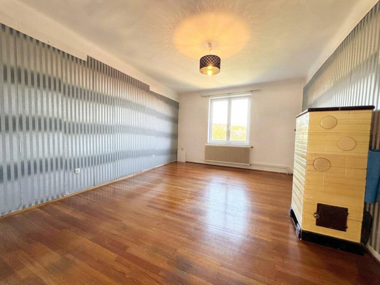 Helles Zimmer mit Holzboden, gestreifter Tapete und einem traditionellen Kachelofen.