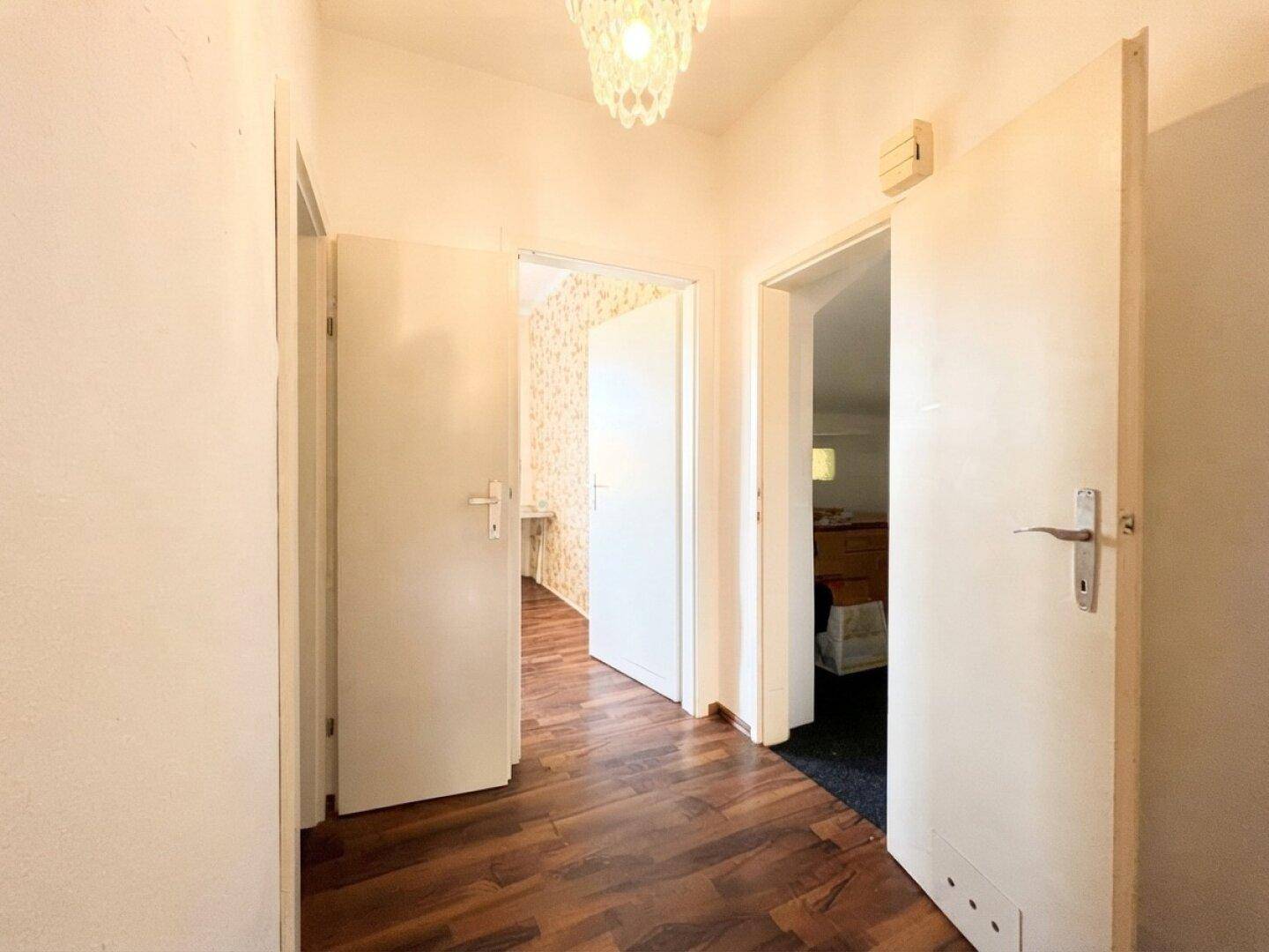 Heller Flur mit dunklem Laminatboden und mehreren Türen, die zu den angrenzenden Räumen führen.