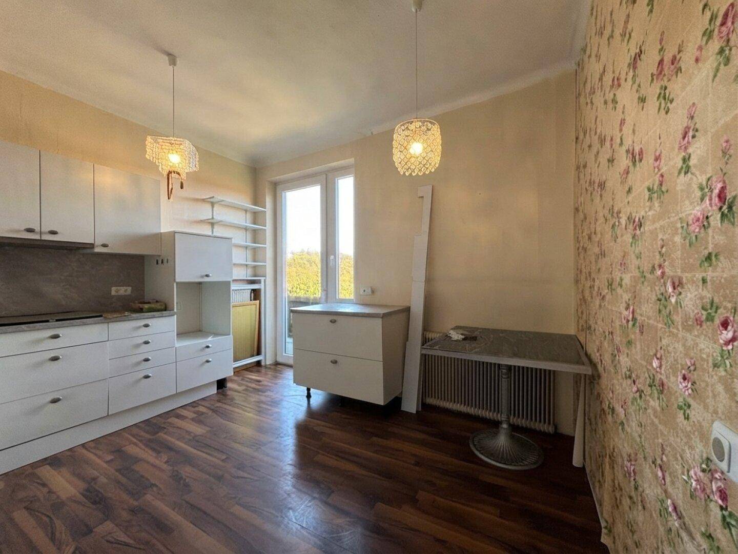 Küche mit weißen Schränken, floraler Tapete und einem Fenster mit Blick ins Grüne.