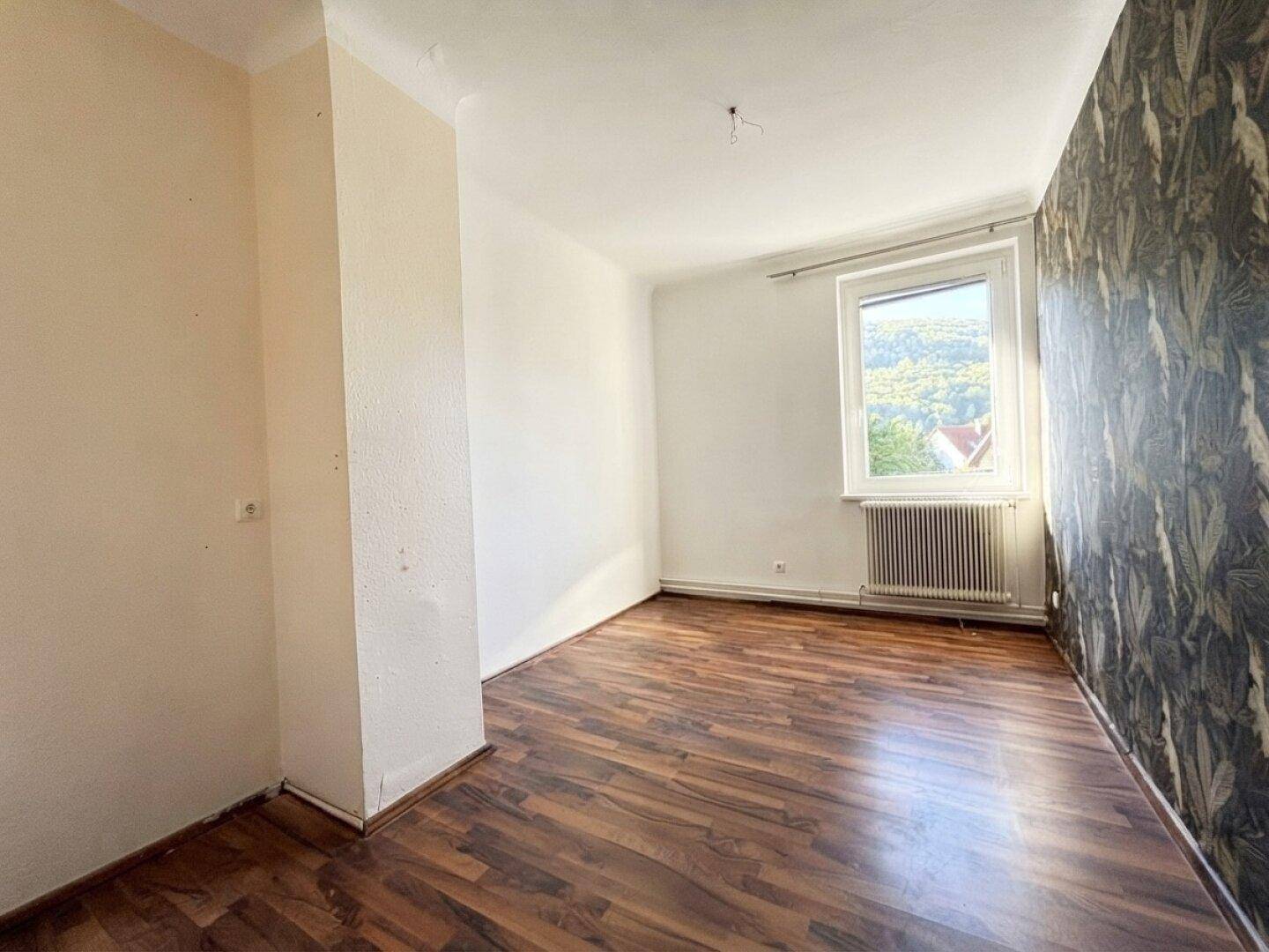 Helles Zimmer mit dunklem Laminatboden und auffälliger tropischer Tapete, Blick ins Grüne.