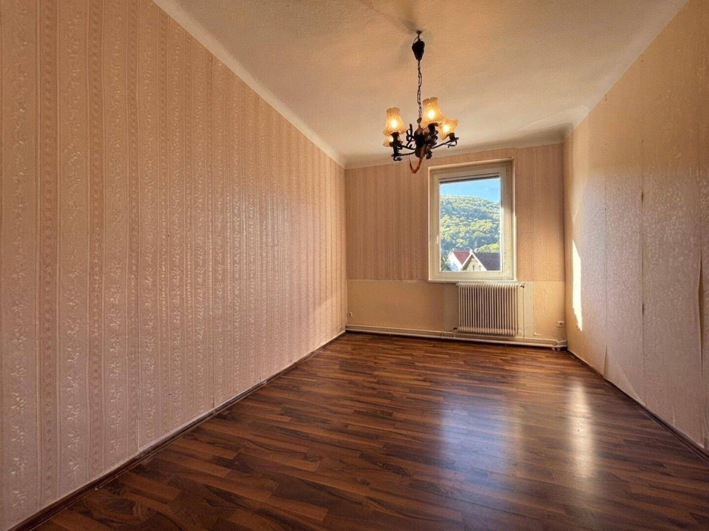 Gemütliches Zimmer mit dunklem Laminatboden, gemusterter Tapete und klassischem Kronleuchter.