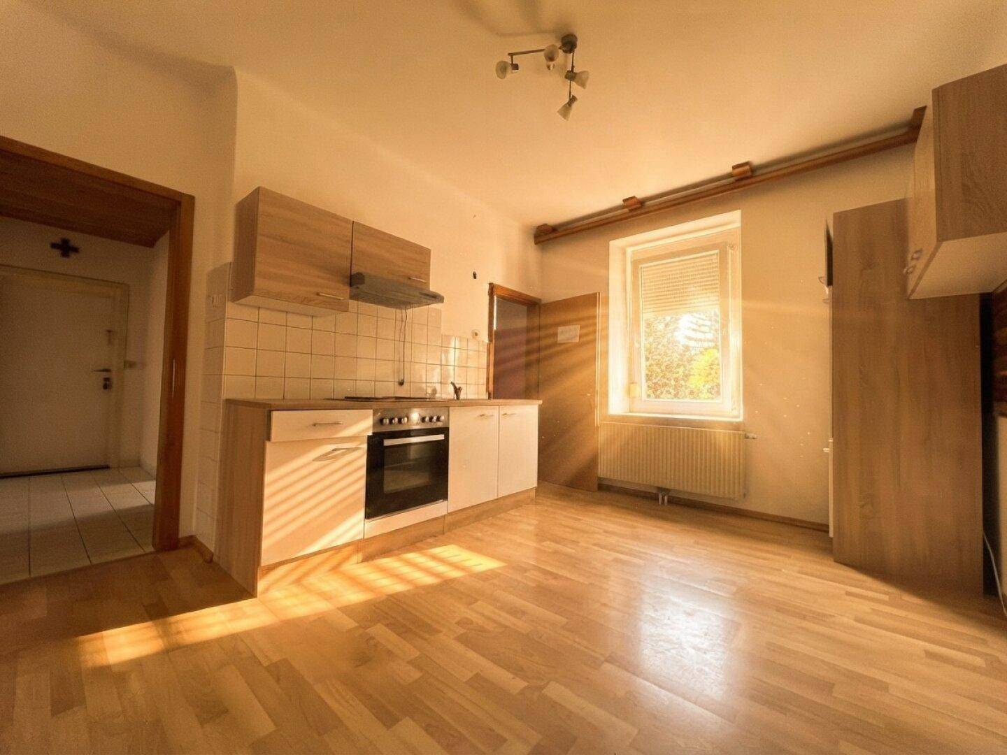 Leere Küche mit einfacher Einbauzeile, Backofen und hellem Laminatboden.