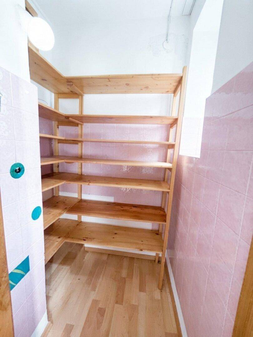 Abstellraum mit Holzregalen und rosa gefliesten Wänden für zusätzlichen Stauraum.