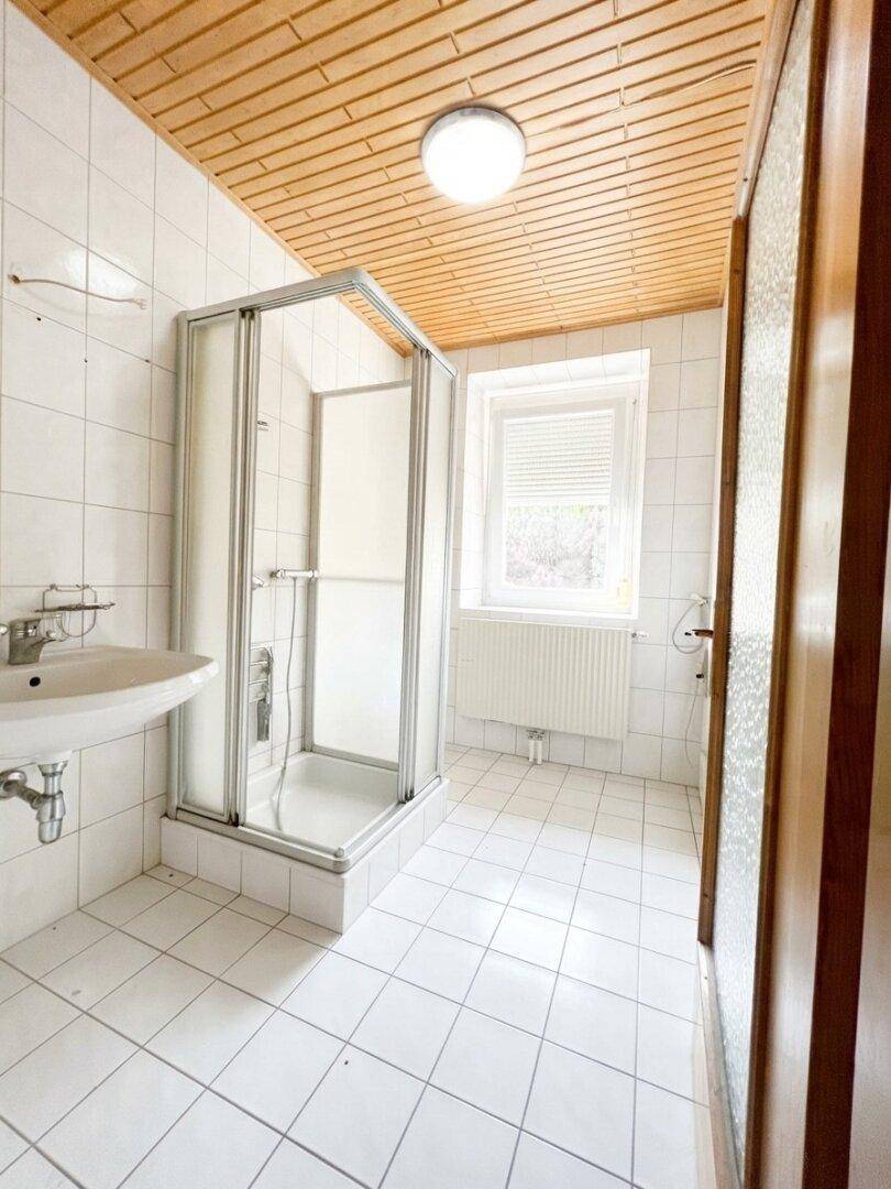 Badezimmer mit Duschkabine, Waschbecken, Fliesen und einer Holzdecke.