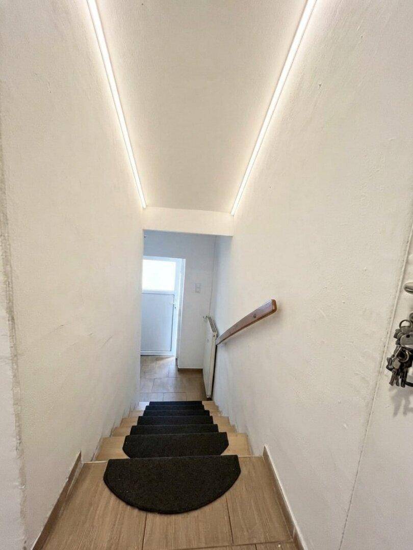 Treppenabgang mit dunklen Stufenmatten und indirekter Beleuchtung an der Wand.