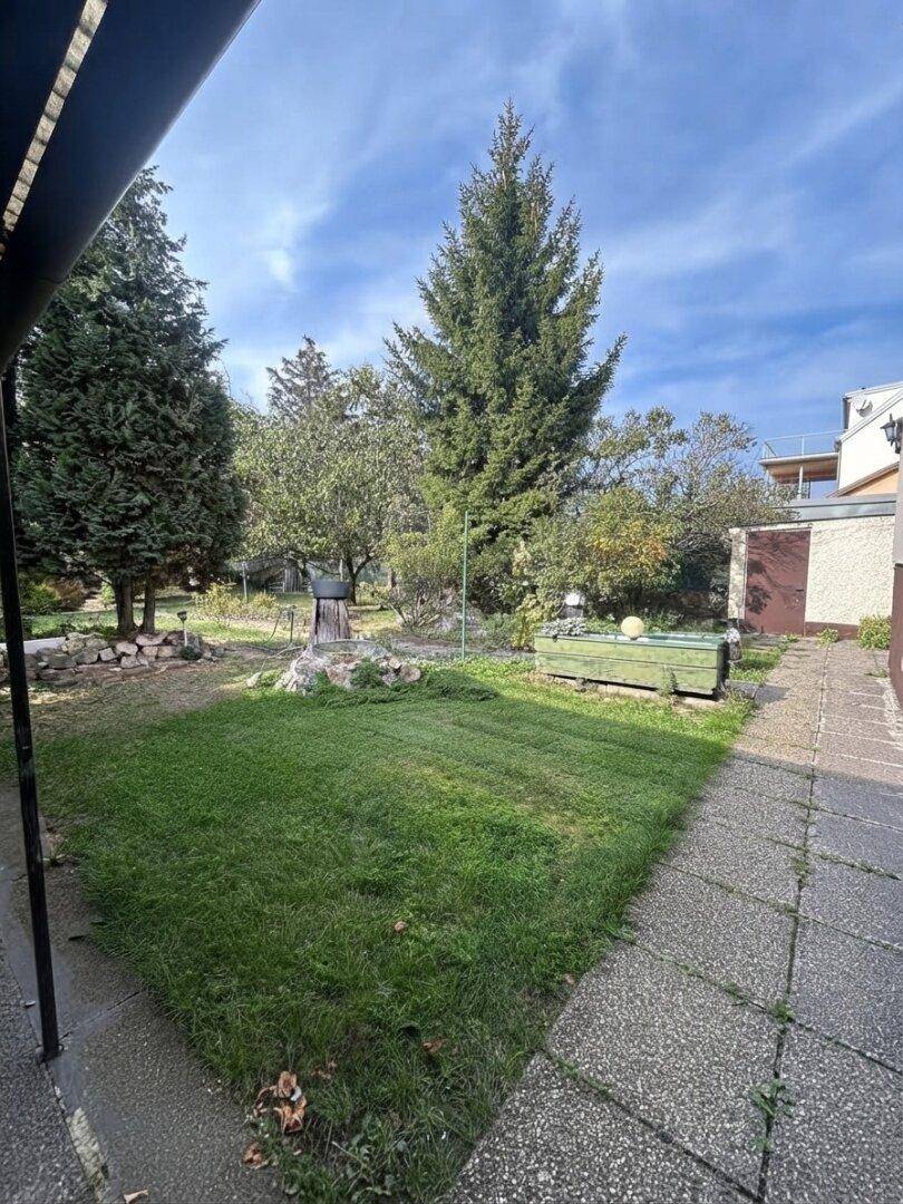 Gartenbereich mit Rasenfläche, gepflastertem Weg und einem kleinen Nebengebäude.