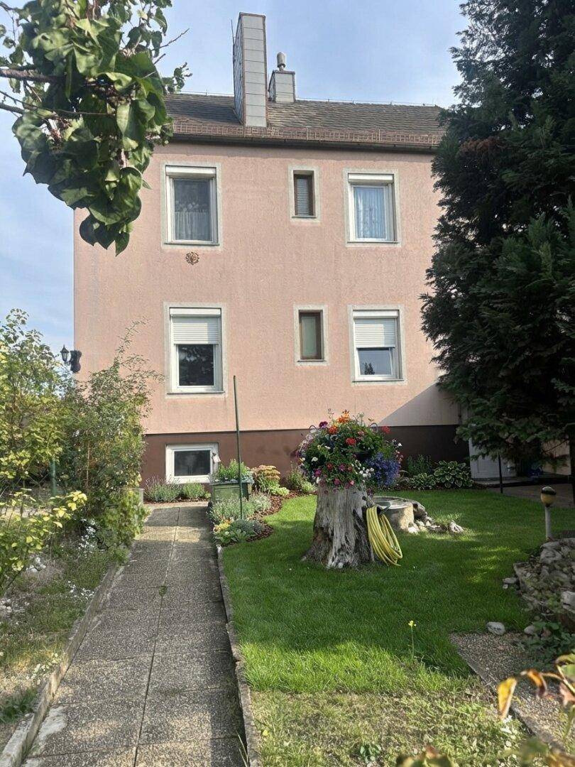 Rückfassade eines rosafarbenen Gebäudes mit mehreren Fenstern und einem gepflegten Garten.
