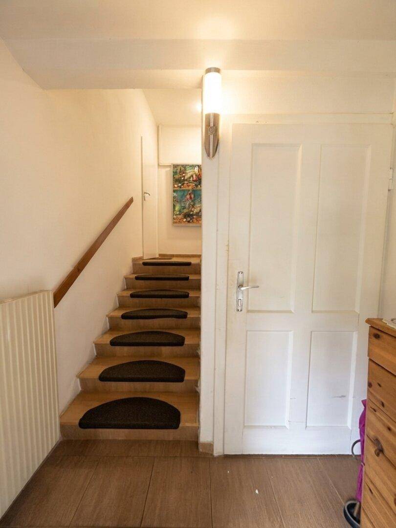 Heller Flur mit Holztreppe, die in das obere Stockwerk führt, und einer weißen Tür.