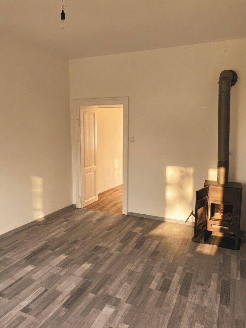 Leerer Raum mit Holzboden und einem traditionellen Holzofen, der Wärme und Gemütlichkeit verspricht.