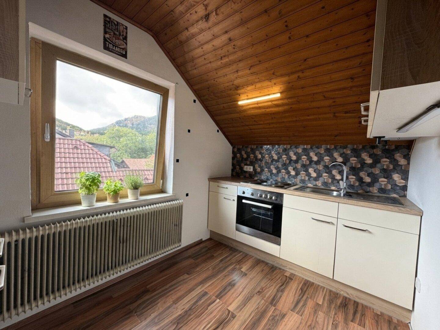 Gemütliche Dachgeschossküche mit Holzbalkendecke, Einbauküche, Ofen und Blick ins Grüne.