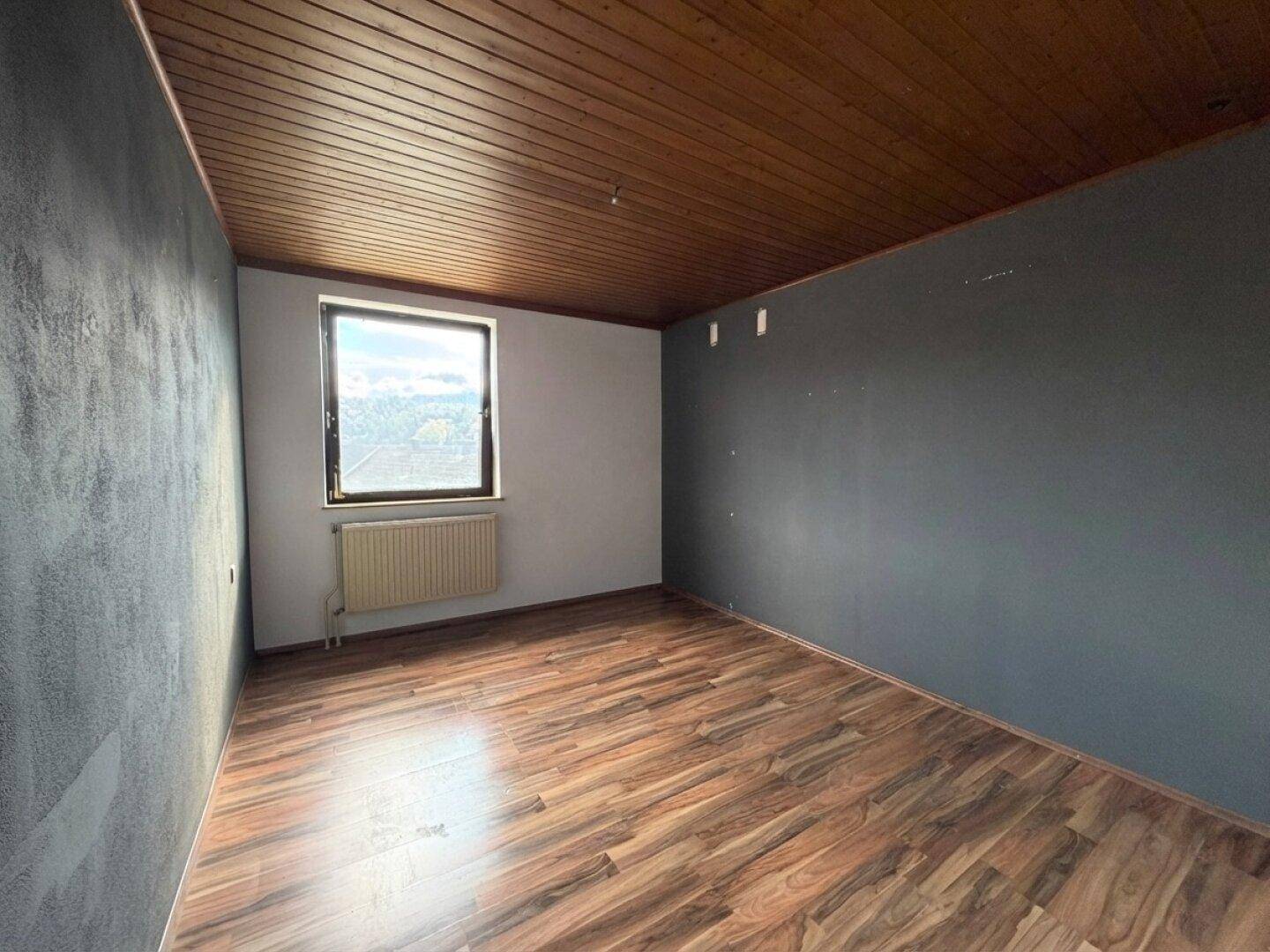 Helles Zimmer mit Laminatboden, Holzbalkendecke und Fenster, ideal als Schlaf- oder Arbeitszimmer.