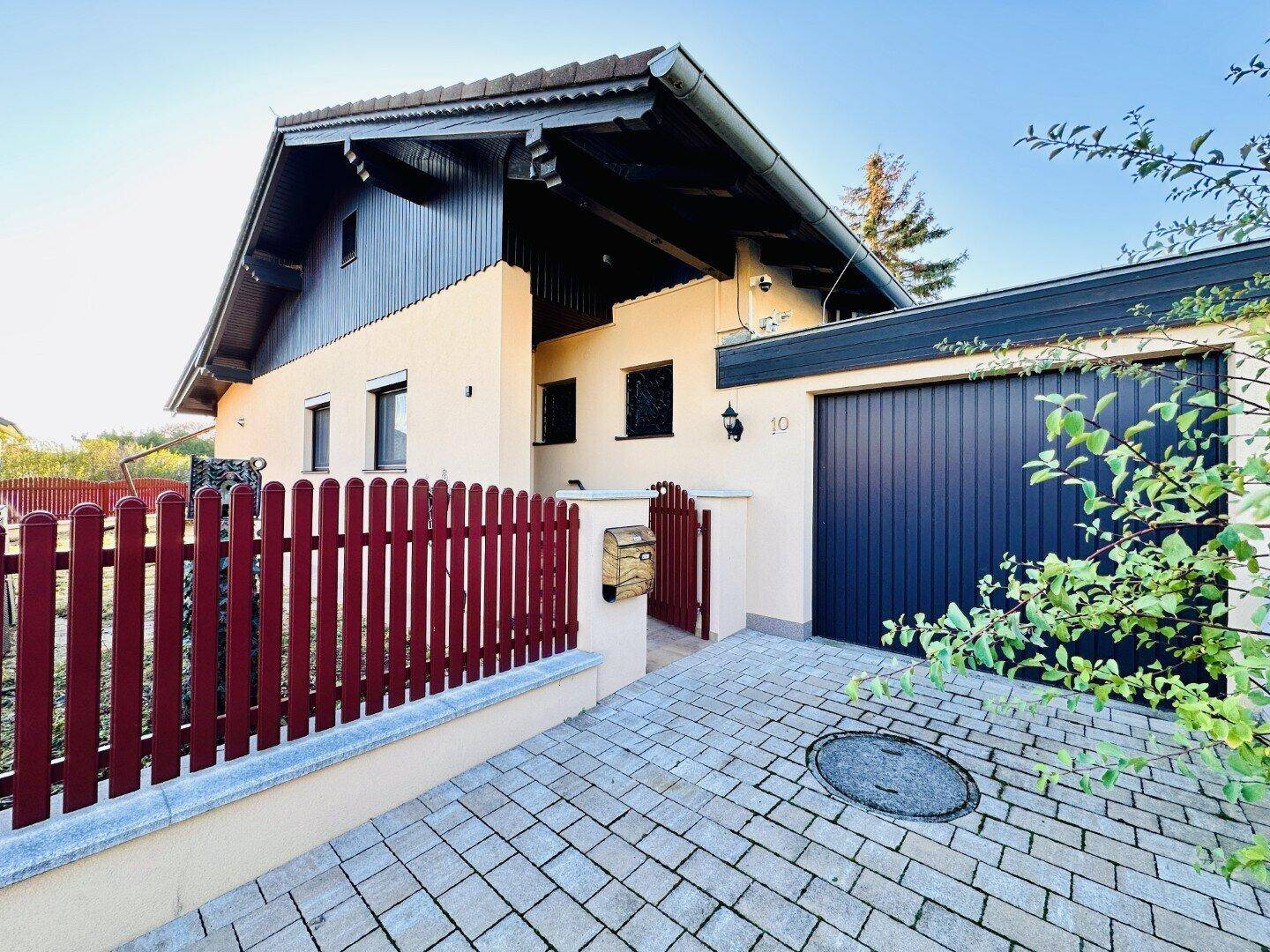Nahaufnahme der Hausfassade mit Einfahrt, Garage und dekorativem Holzzaun.