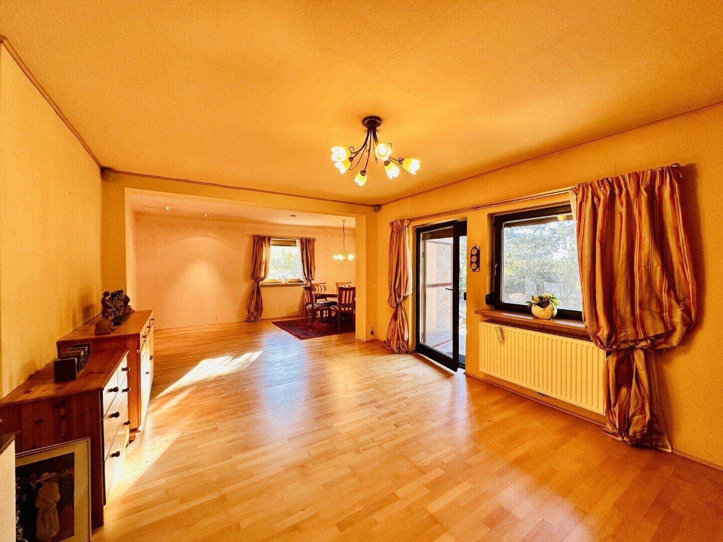 Heller Wohn- und Essbereich mit Holzboden und Zugang zur Terrasse durch eine Glastür.