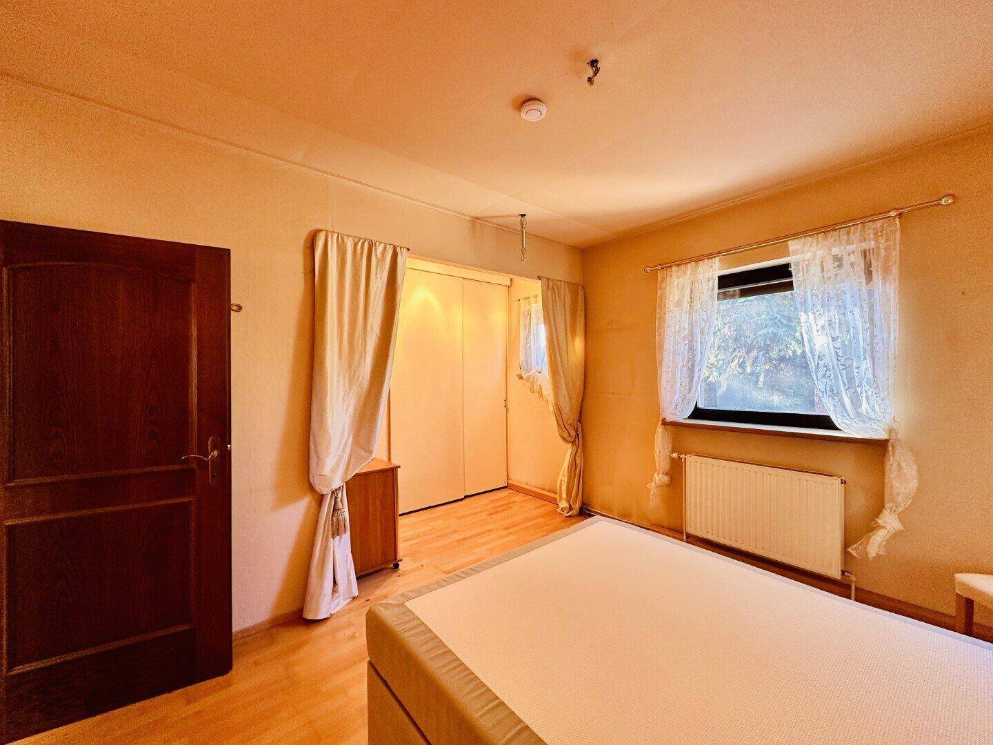 Schlafzimmer mit Holzboden, Einbauschränken und Fenster mit Vorhängen.