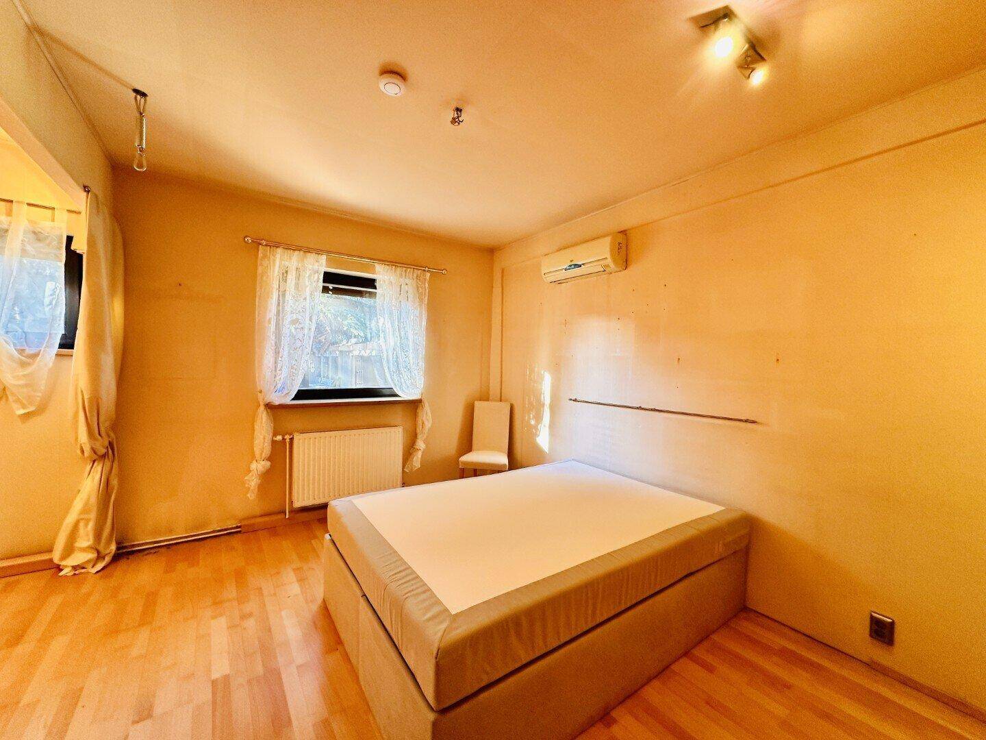 Schlafzimmer mit Holzboden, Doppelbett und Klimaanlage an der Wand.