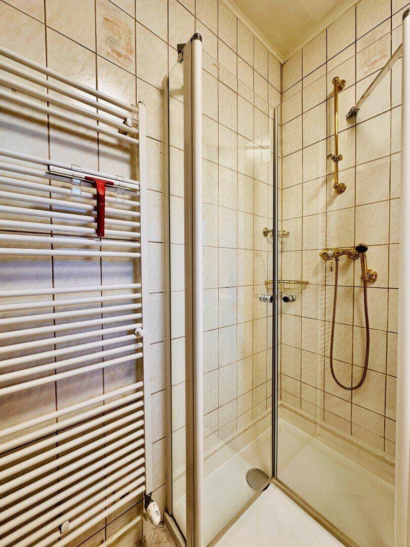 Duschbereich im Badezimmer mit Fliesen, Glasabtrennung und Handtuchheizkörper.