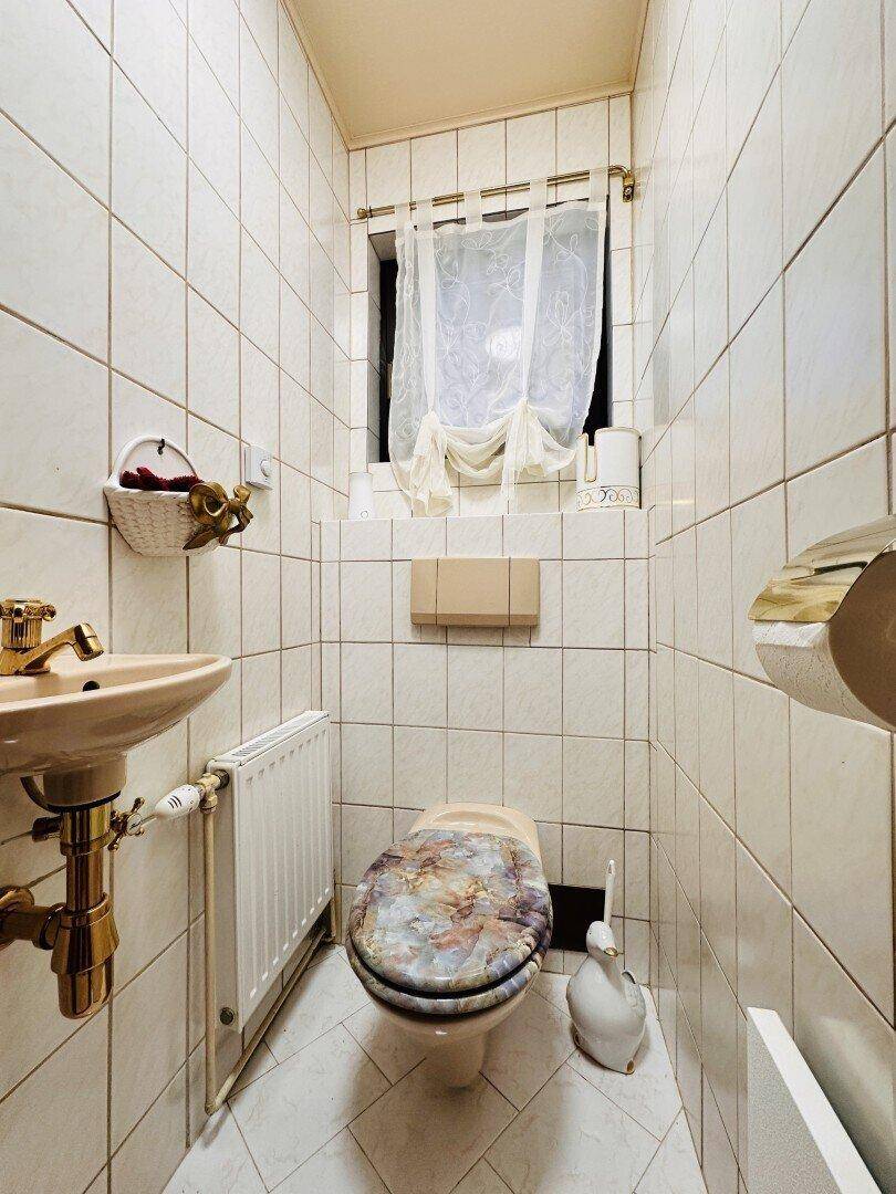 Separate Toilette mit Fliesen, kleinem Waschbecken und Fenster.