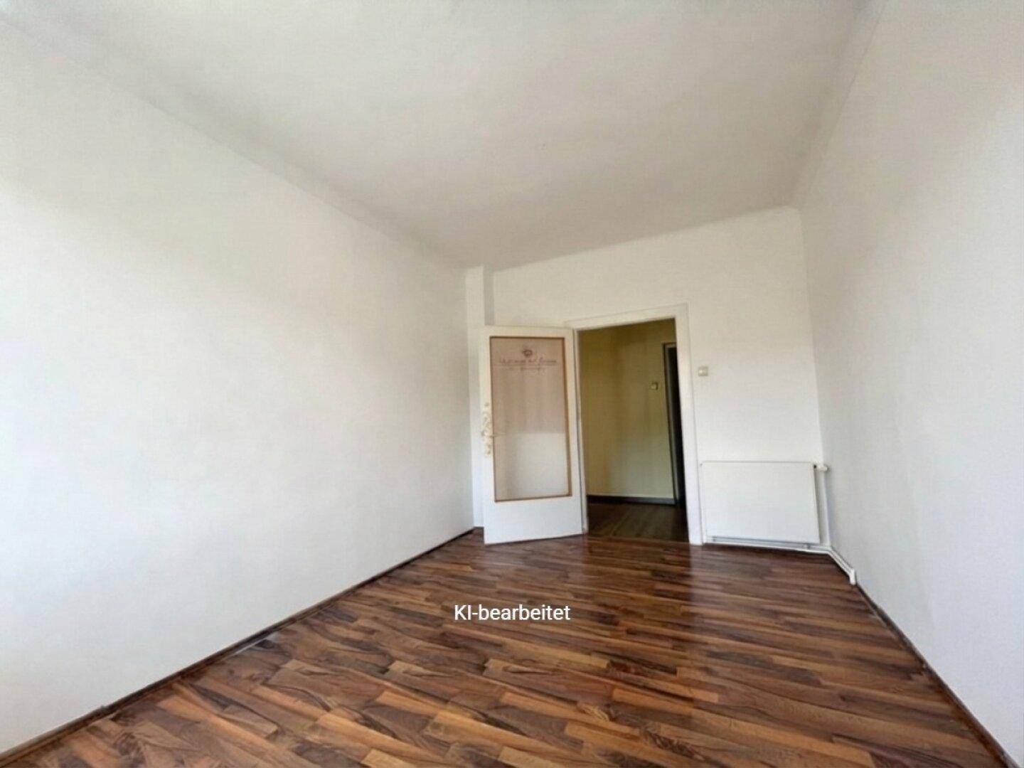 Leeres Zimmer mit Laminatboden und einer Tür, die zu einem anderen Bereich führt.