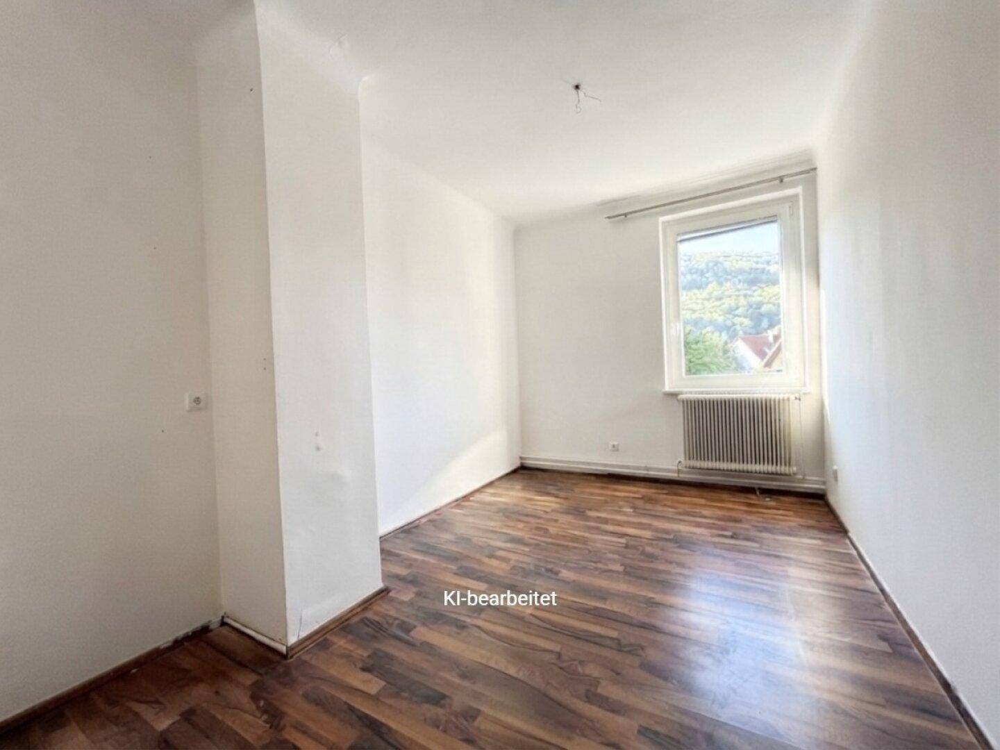 Kleines, helles Zimmer mit Laminatboden und einem Fenster mit Blick ins Grüne.