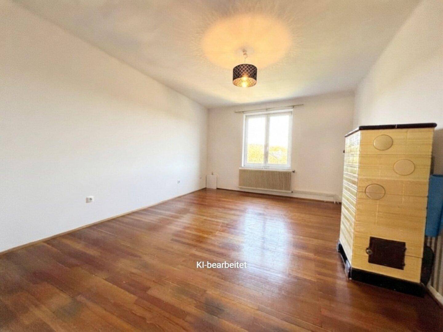Helles Zimmer mit Holzboden und einem traditionellen Kachelofen als Heizelement.