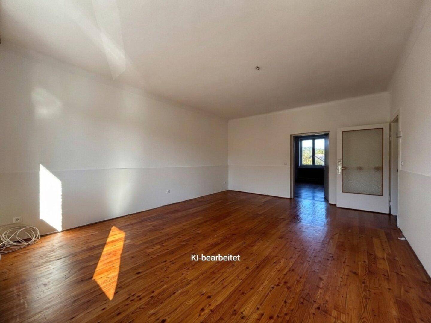 Geräumiges, helles Zimmer mit Holzboden und Zugang zu einem weiteren Raum.