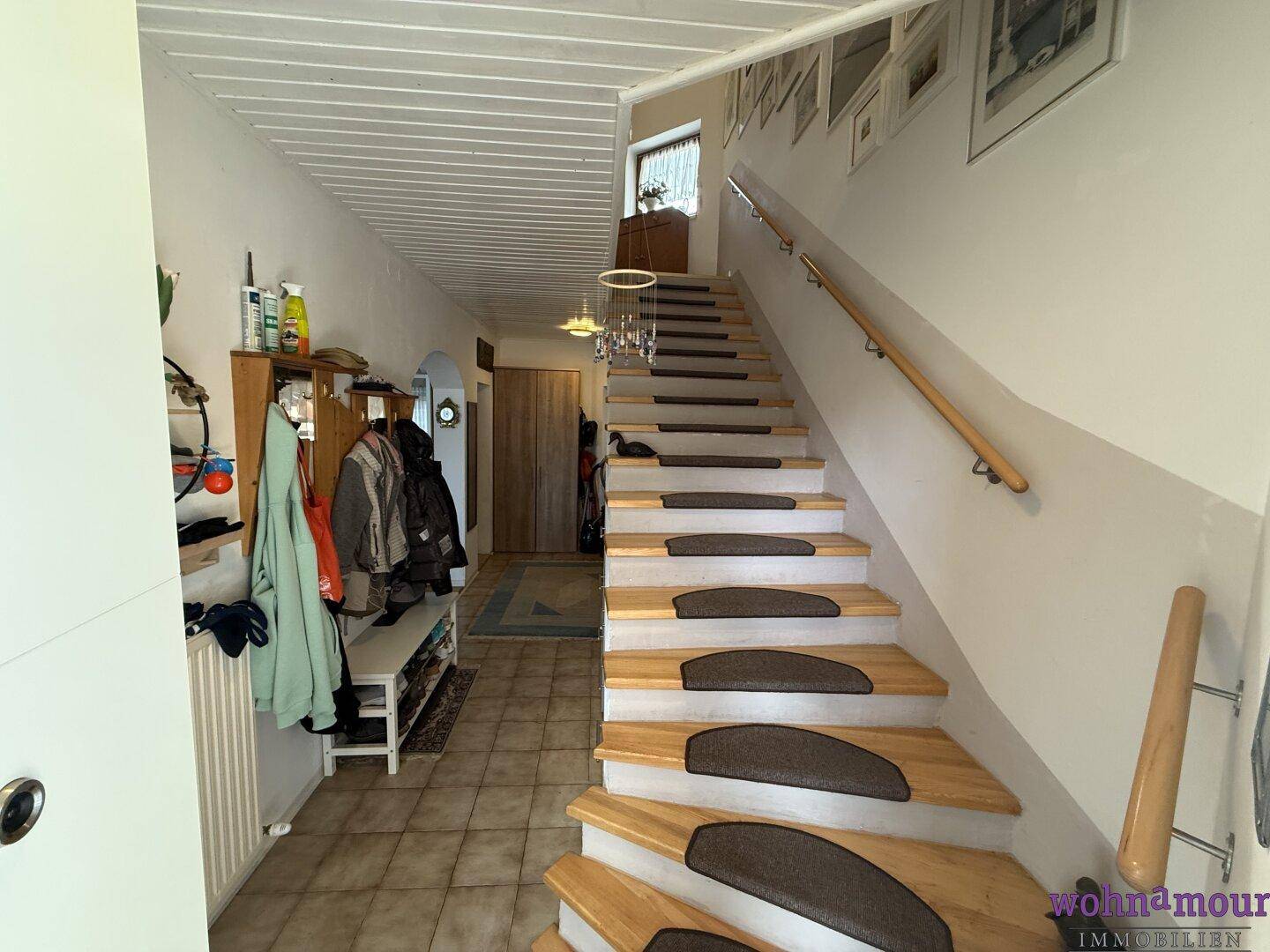 Heller Eingangsbereich mit Holztreppe und Garderobe, führt zu den oberen Etagen.