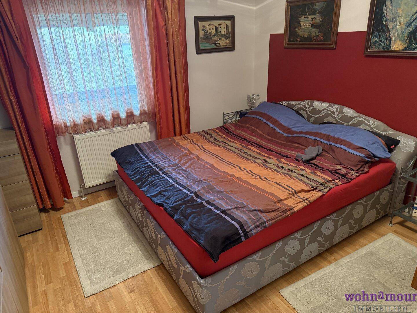 Gemütliches Schlafzimmer mit Doppelbett, Holzfußboden und Fenster mit Vorhängen.
