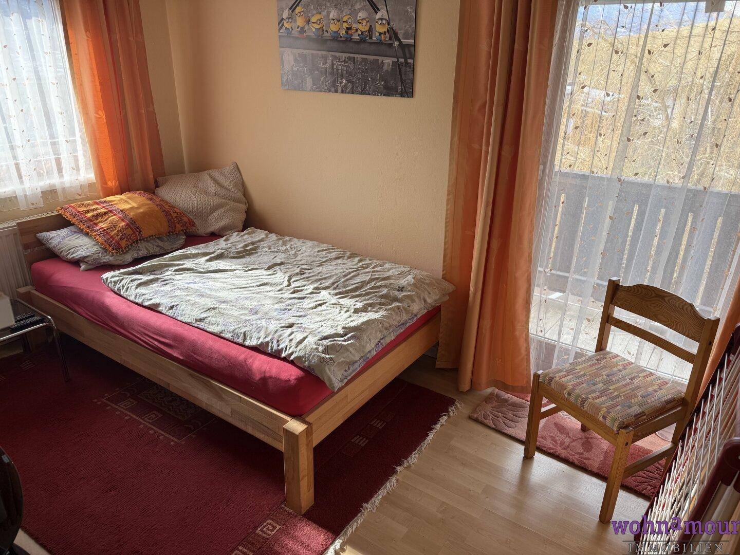 Helles Schlafzimmer mit Einzelbett, Holzboden und Zugang zu einem Balkon.