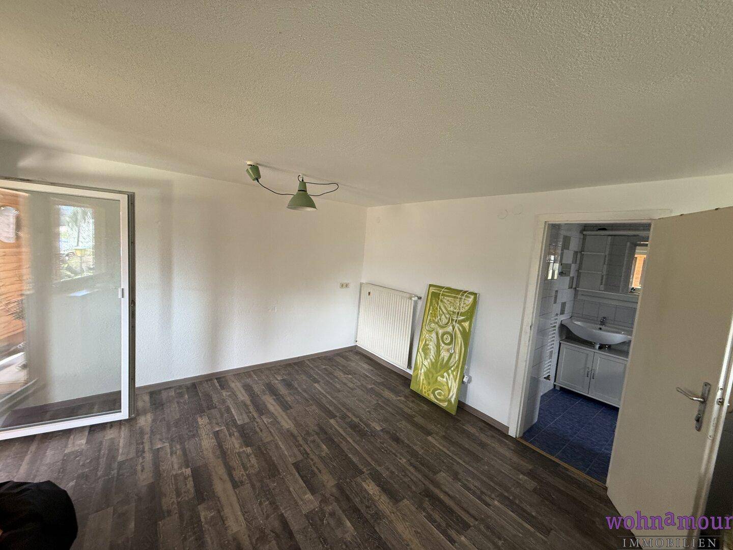 Leerer Raum mit dunklem Laminatboden und Zugang zu einem Balkon oder einer Terrasse.