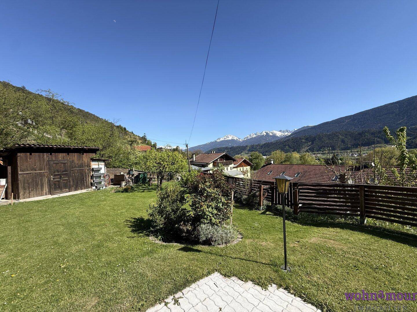 Weitläufiger Garten mit Rasenfläche, Gartenhaus und Panoramablick auf die Berge.