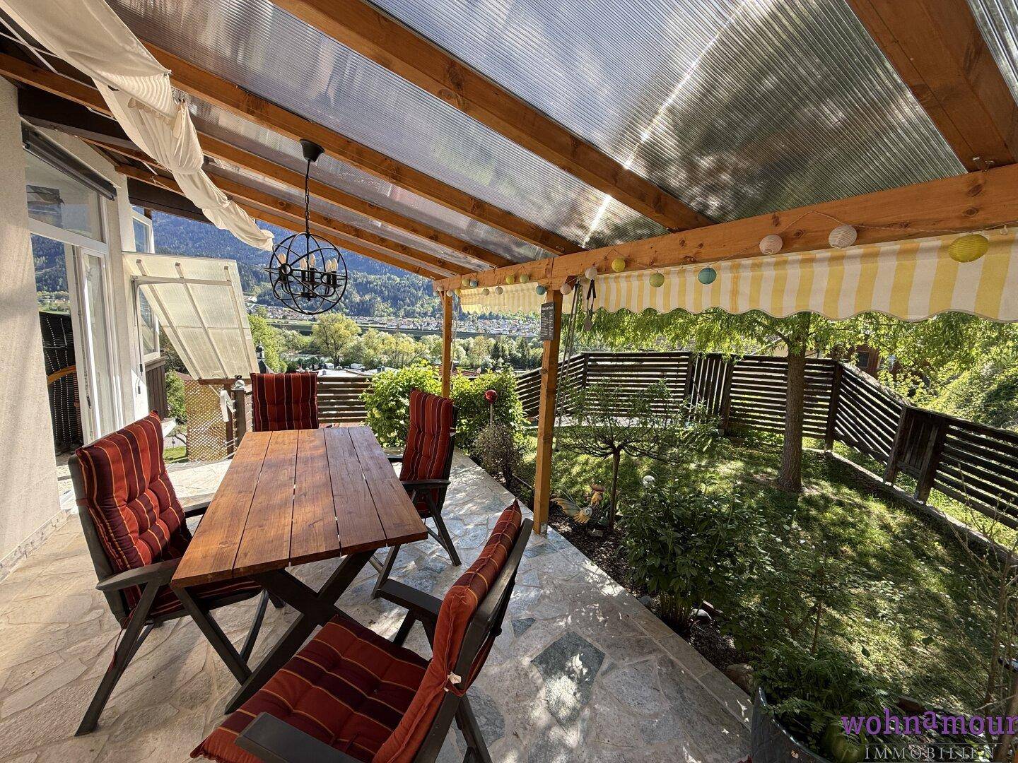 Überdachte Terrasse mit Holztisch und Stühlen, ideal für Mahlzeiten im Freien mit Bergblick.