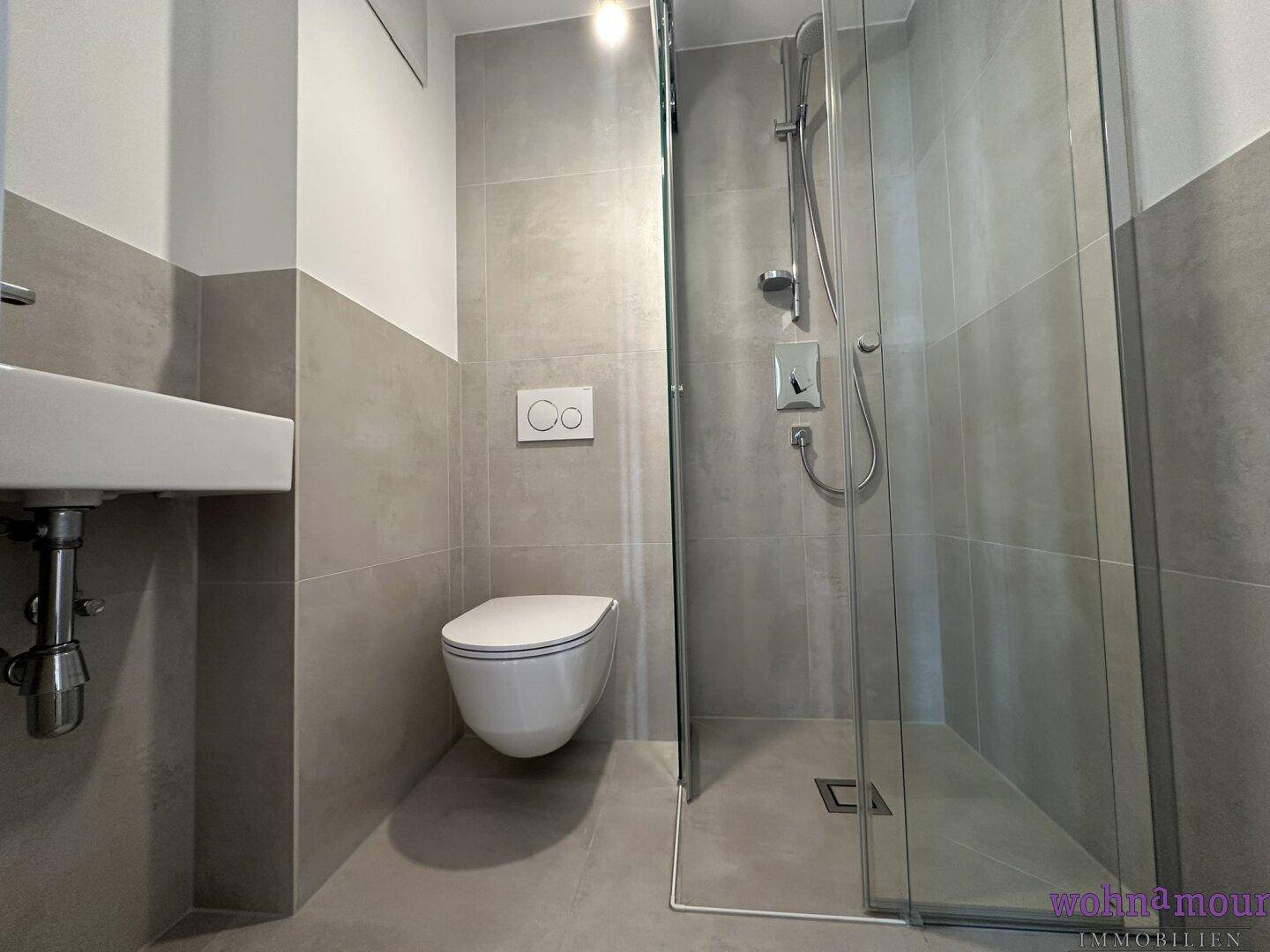 Zeitgemäßes Badezimmer mit ebenerdiger Dusche, wandhängendem WC und stilvollen grauen Fliesen.