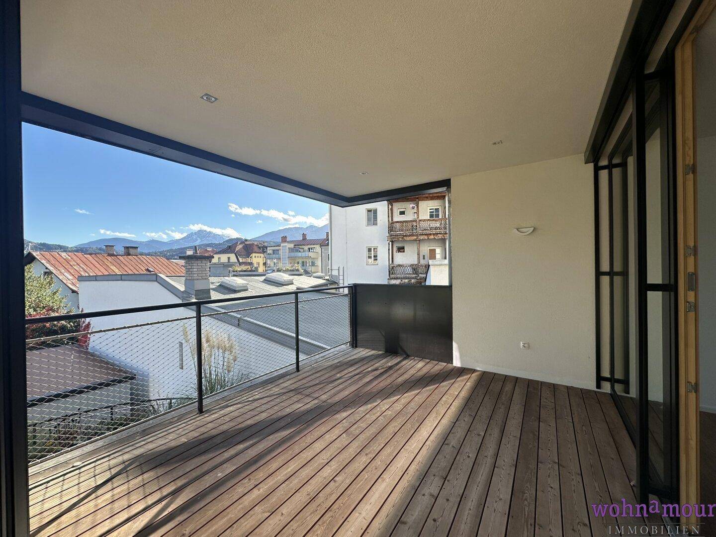 Geräumiger Balkon mit Holzboden und Blick auf die umliegende Stadt und die Berge.