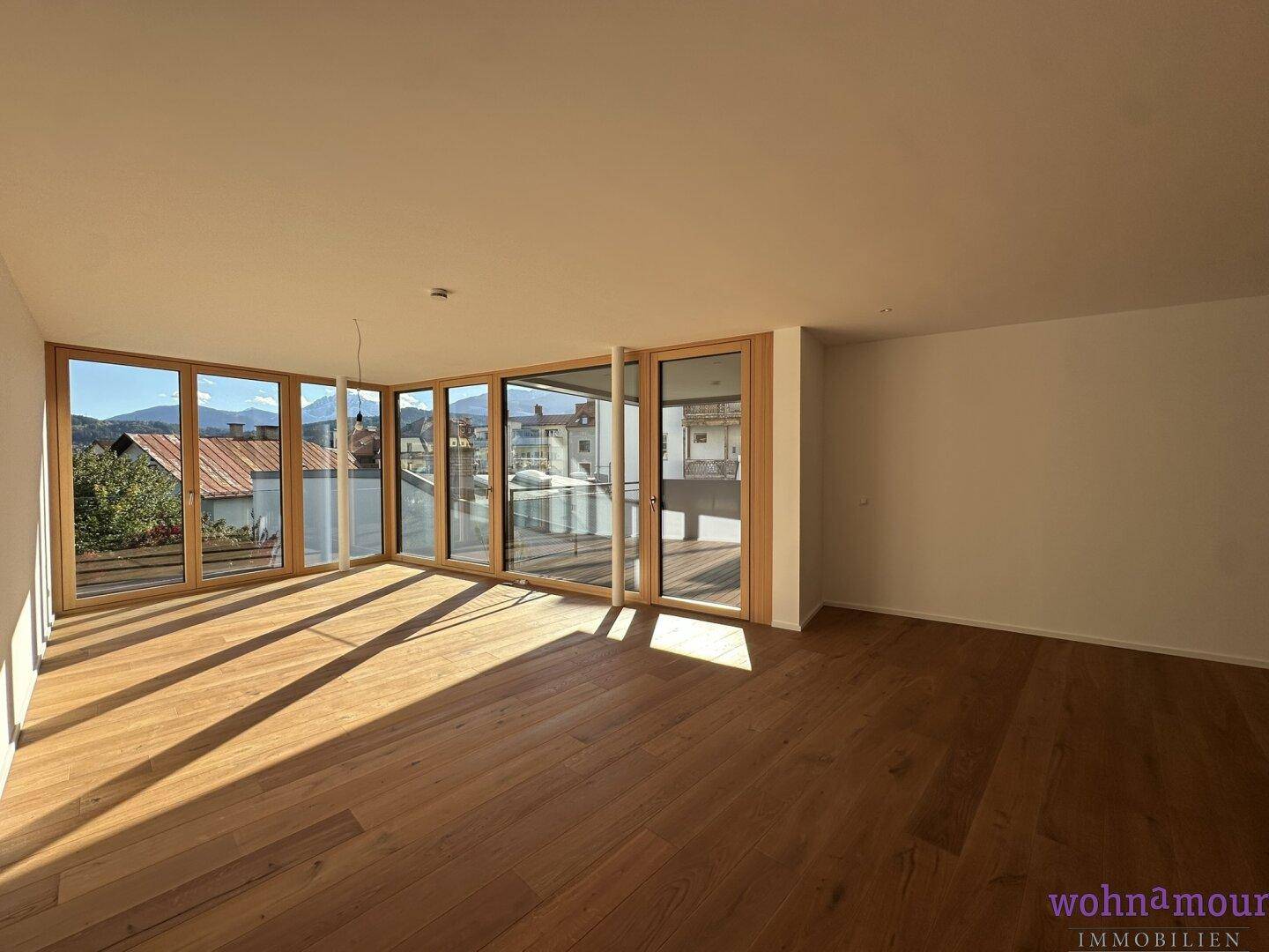 Lichtdurchfluteter Wohnraum mit elegantem Holzboden und großen Fensterfronten, die viel Tageslicht hereinlassen.